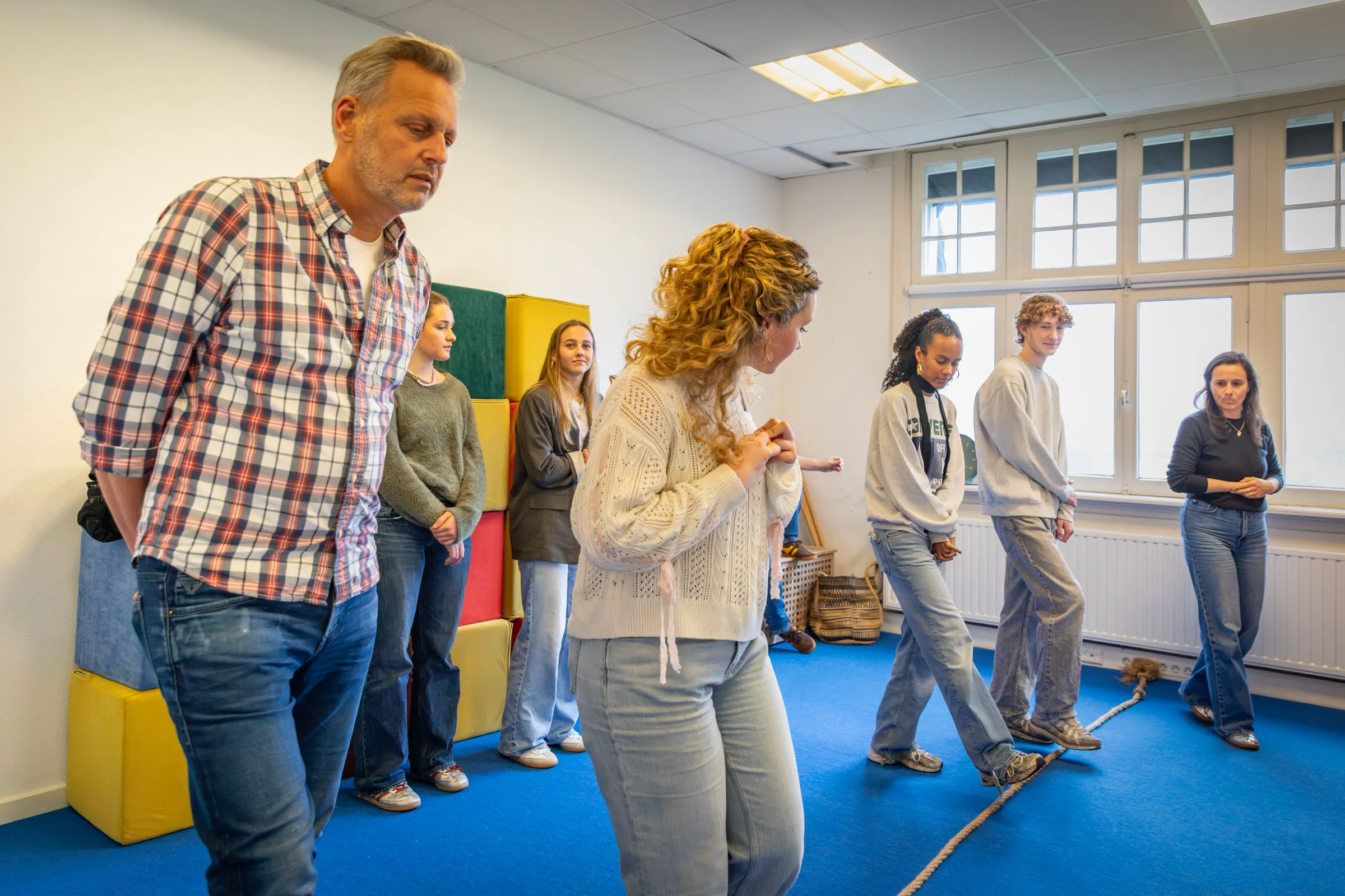 Deelnemers lopen geconcentreerd langs een touw op de grond tijdens groepsoefening