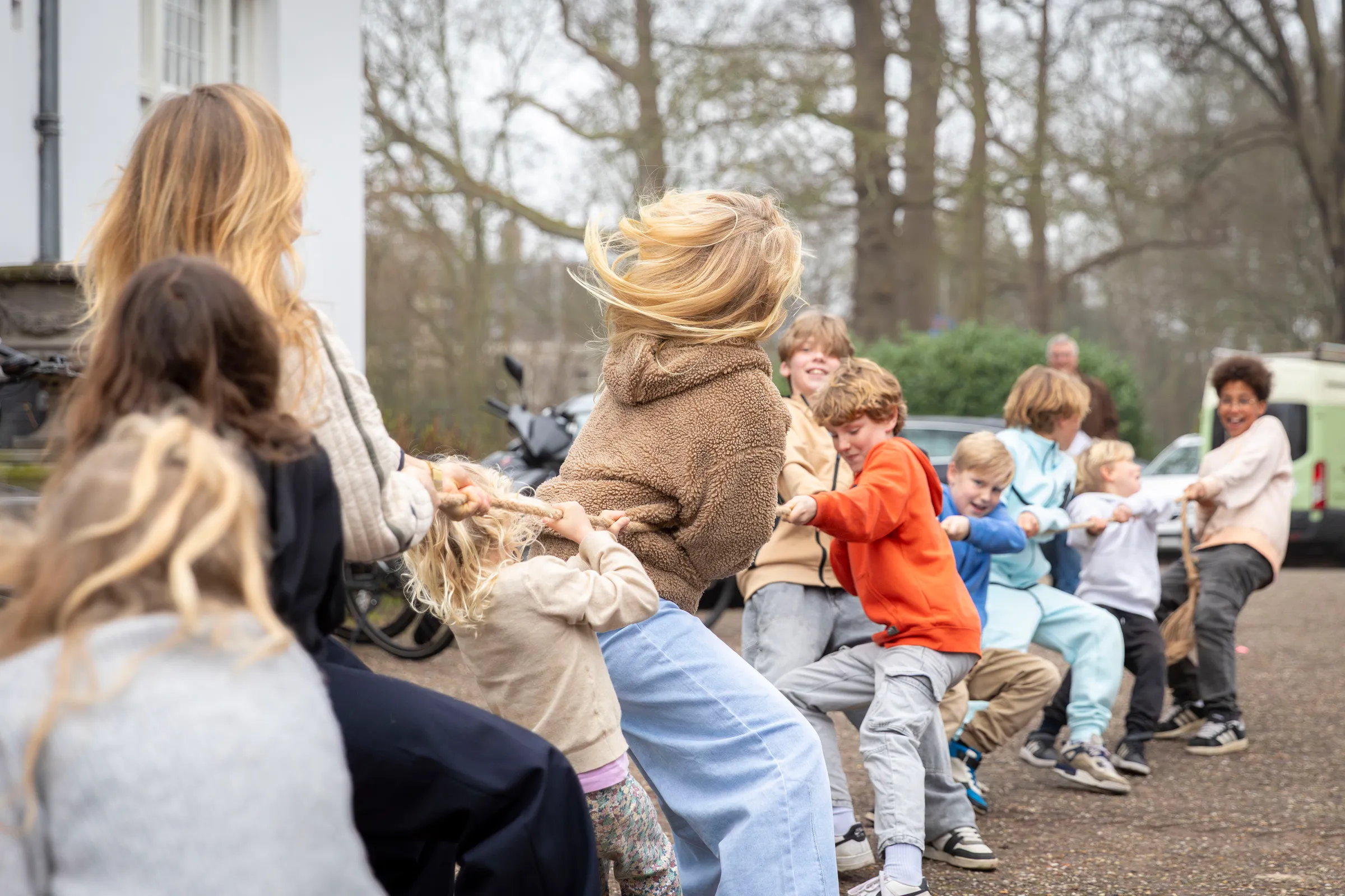 Kinderen en jongeren spelen touwtrekken buiten bij Het Huis