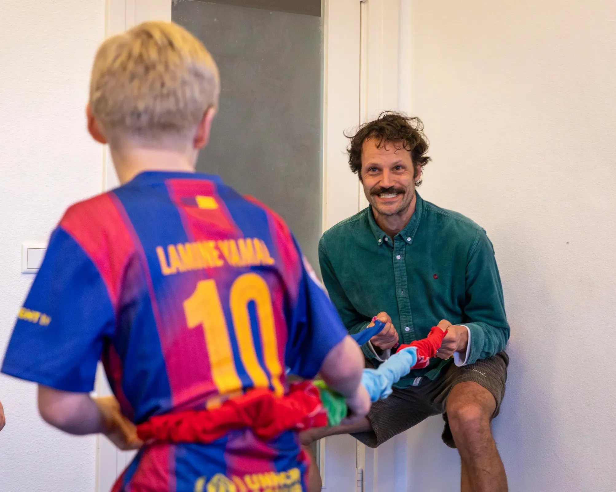 Jongen kijkt naar therapeut die kleurrijke doeken vasthoudt in therapieruimte