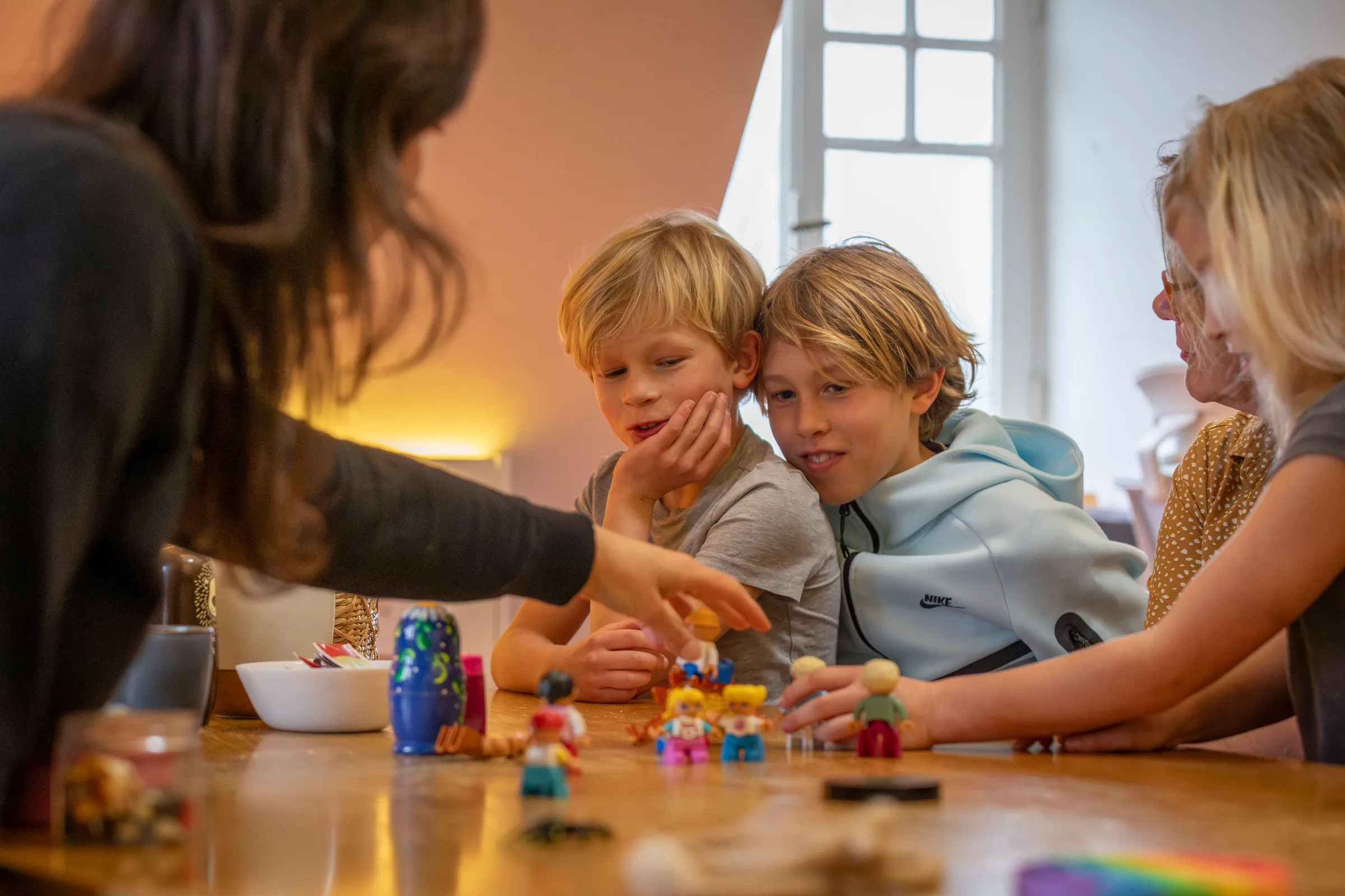 Twee jongens kijken gefocust naar speelfiguurtjes terwijl therapeut iets aanwijst